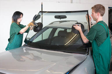 Two people installing a new car windshield.
